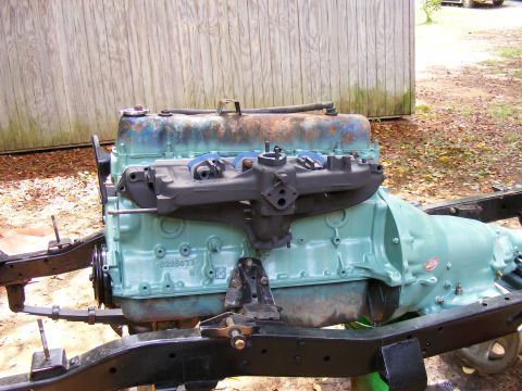 Engine and transmission assembly on a frame. Engine is teal with a black intake manifold. Transmission is also