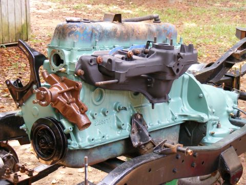 Engine block painted light blue, with a brown water pump and black intake manifold attached. Some frame compon