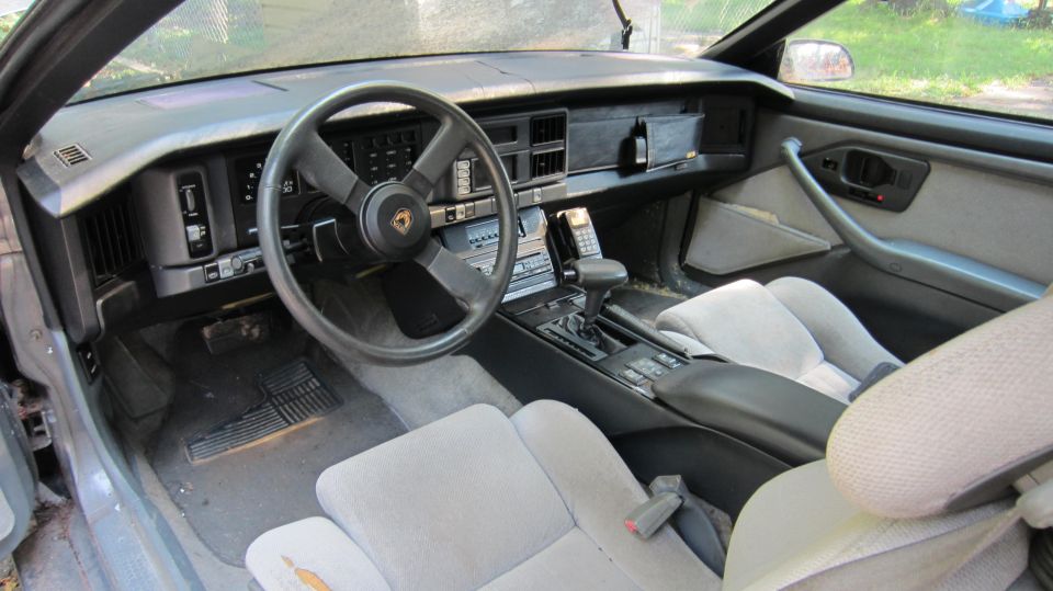 1987 Pontiac Firebird interior with grey cloth seats, dashboard, steering wheel, and center console
