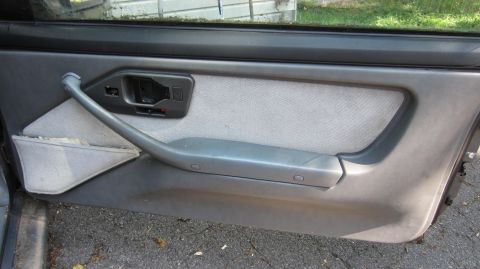 1987 Pontiac Firebird - The interior door panel of a 1987 Pontiac Firebird shows gray fabric and a silver handle.