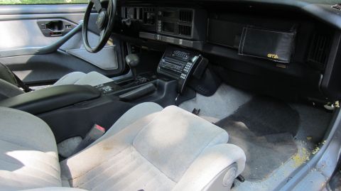 1987 Pontiac Firebird - Interior view of a 1987 Pontiac Firebird, light grey seats and a black dashboard with a GTA emblem.