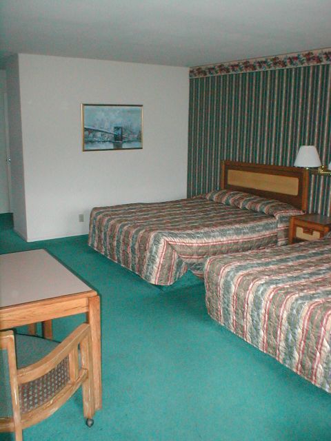 1994 Ford Crown Victoria - This hotel room scene features two beds, a desk, and a painting of a bridge on the wall. The Supermotors.net logo is visible.