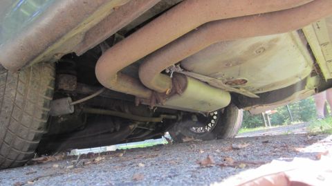 1987 Pontiac Firebird - A low-angle shot reveals the exhaust system and undercarriage of a vehicle, with a portion of the rear tire visible.