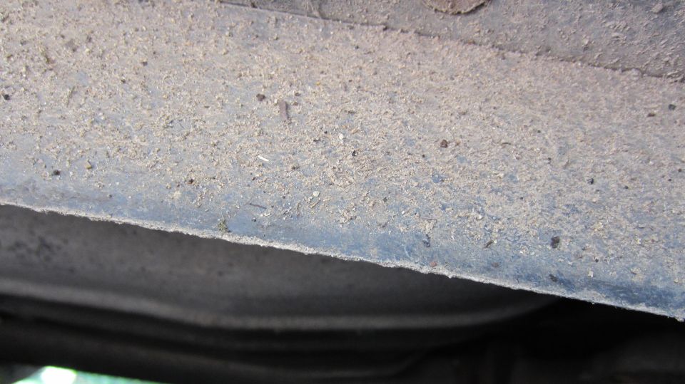 close-up of the dusty underside of a car, showing the frame and some dirt buildup