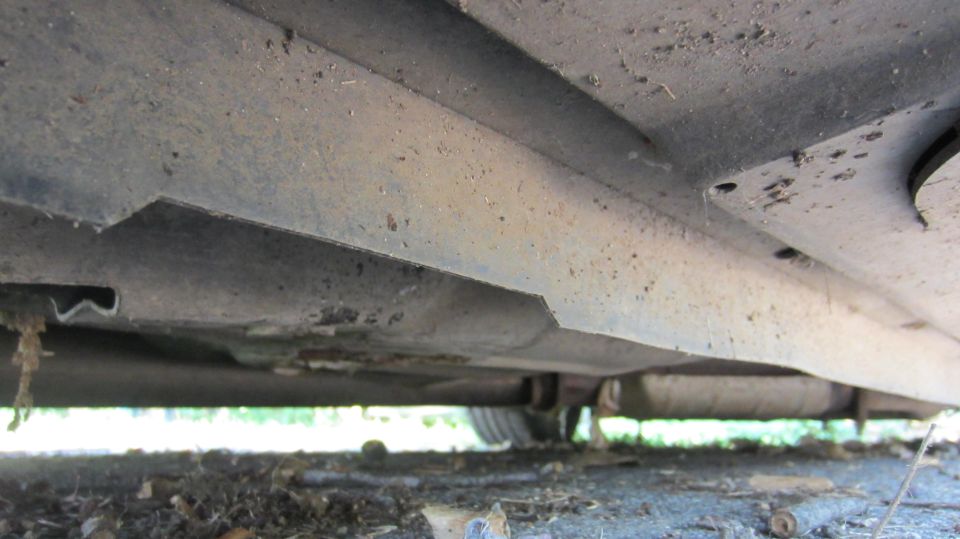 Underside of a dirty car, showing the rocker panel, exhaust pipe, and a tire in the distance