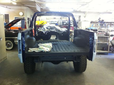 1982 Ford Bronco - This stripped-down blue Ford Bronco is in a workshop, showing its rear end and bed.
