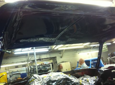 1982 Ford Bronco - Two people are working on a car interior, with another vehicle visible in the background of the shop.