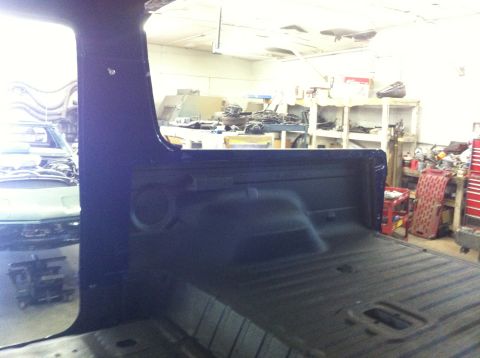 1982 Ford Bronco - View from inside a dark blue pickup truck, showing the bed and cab interior, with another vehicle in the background workshop.