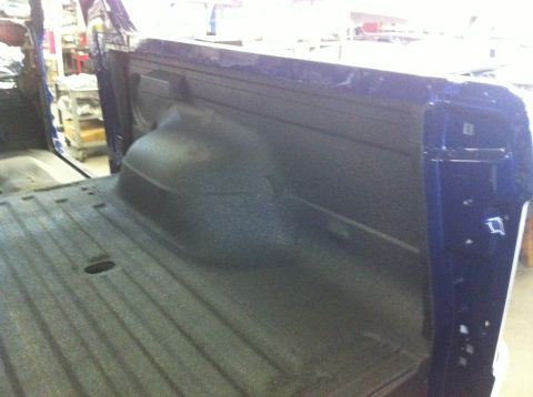 1982 Ford Bronco - The interior of a blue pickup truck's bed, a textured spray-in liner and the rear wheel well.