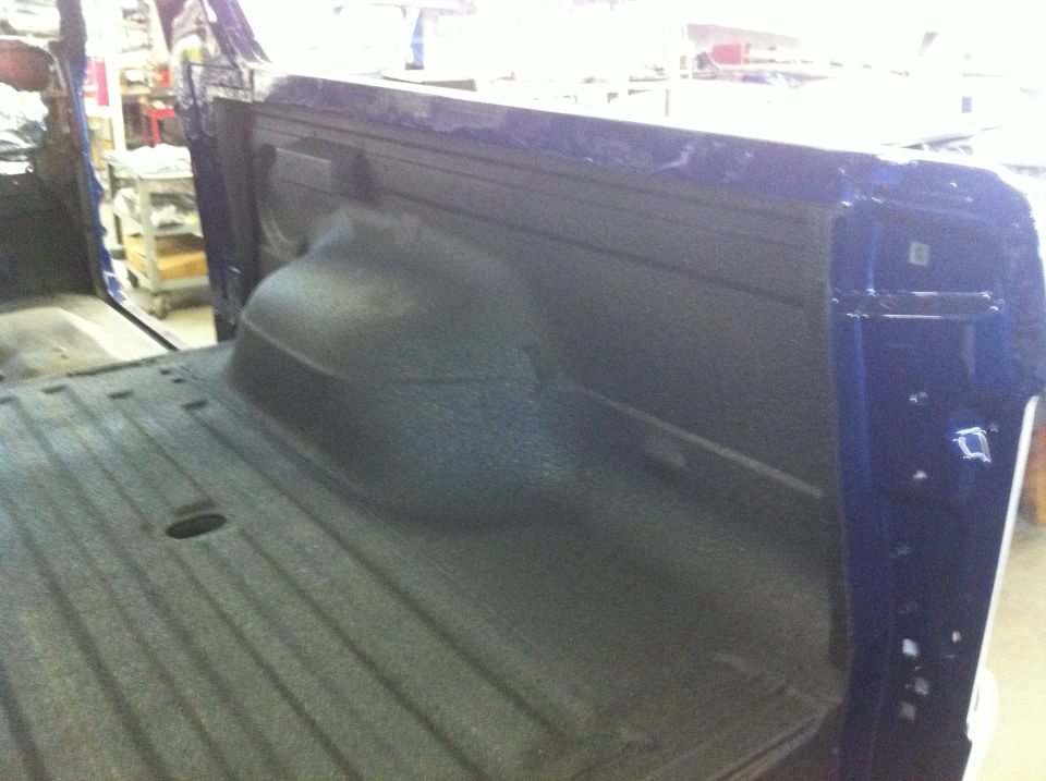 Blue truck bed with spray-in liner. Shows wheel well and tailgate area
