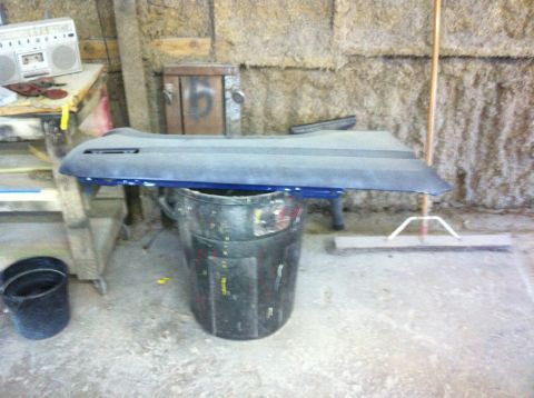 1982 Ford Bronco - A blue car door panel is placed on a trash can in a cluttered garage setting.