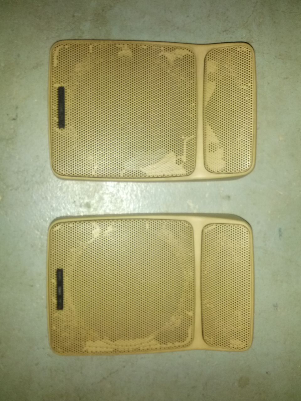 Two tan speaker grilles with perforated covers and some damage