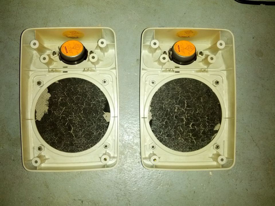 Two beige car speaker housings with torn black mesh and orange drivers, viewed from the back