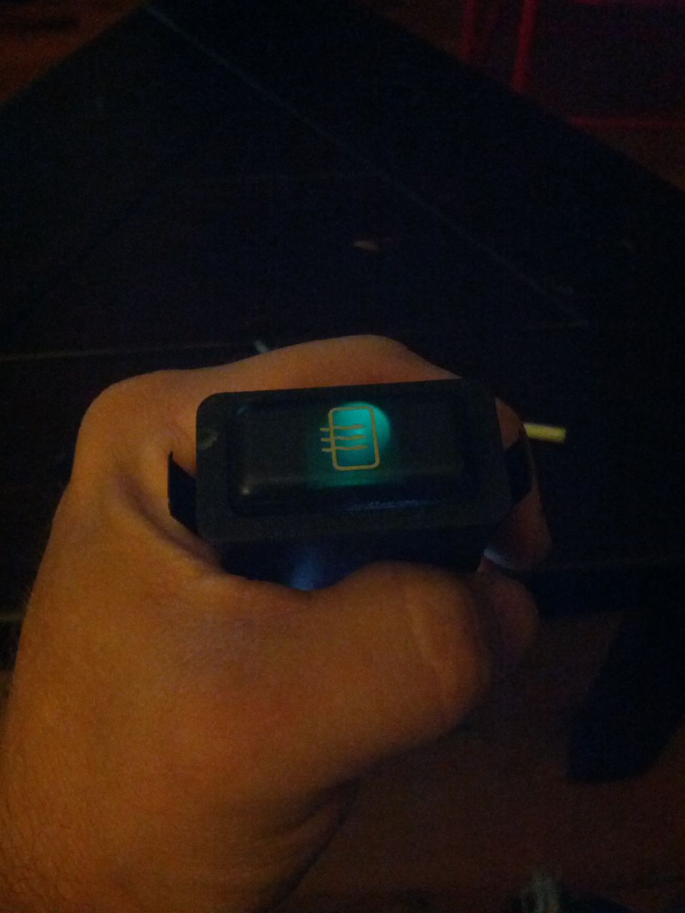Hand holding a car interior light switch with a glowing icon