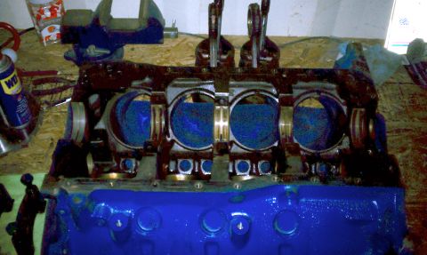 1996 Ford Bronco - Engine block assembly with pistons and connecting rods, partially painted blue, on a wooden surface.