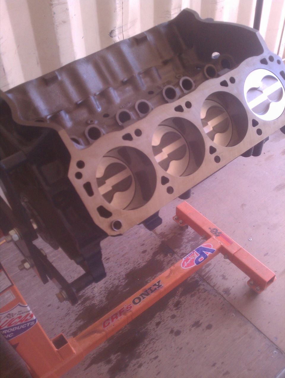 Engine block with pistons on an orange engine stand, text visible on stand