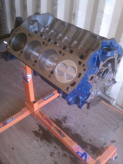 1996 Ford Bronco - A blue engine block with pistons is mounted on an orange engine stand, ready for assembly.