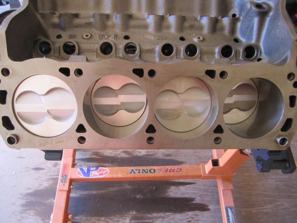 Engine block with four pistons visible, mounted on an orange stand