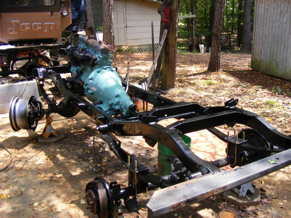 Jeep frame with engine and transmission installed, wheels off, on jack stands outdoors