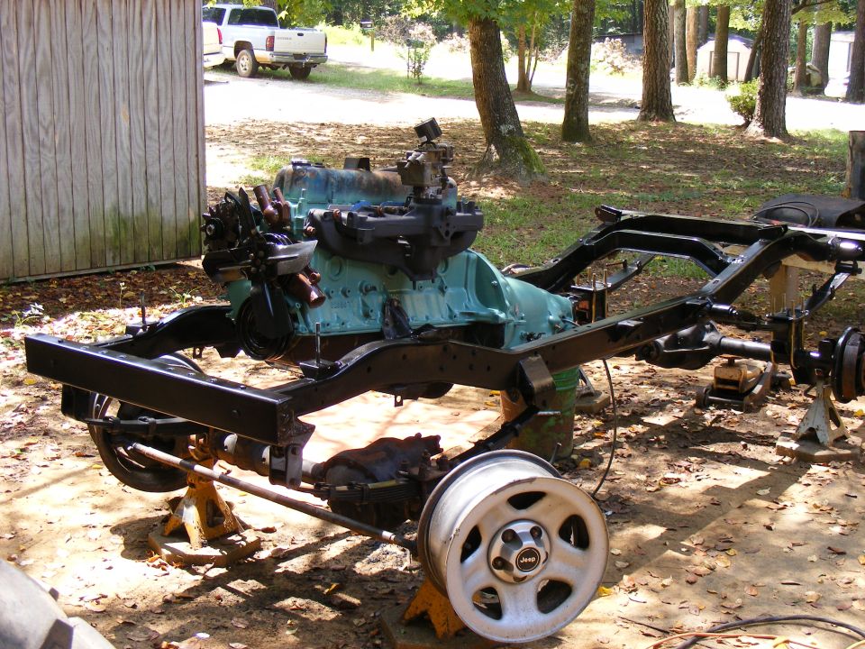 Vehicle frame with engine and a white pickup truck in the background