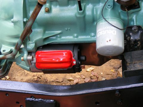 Engine starter motor with red cover and oil filter on a green engine block