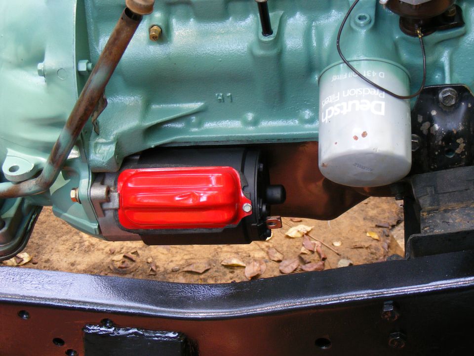 Engine starter motor with red cover and oil filter on a green engine block