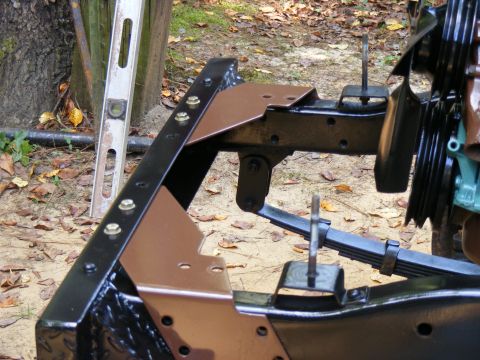 Close-up of vehicle frame with leaf springs and mounting brackets. A level is visible to the left