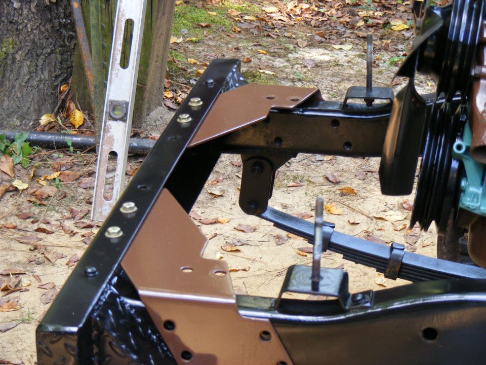 Close-up of vehicle frame with leaf springs and mounting brackets. A level is visible to the left