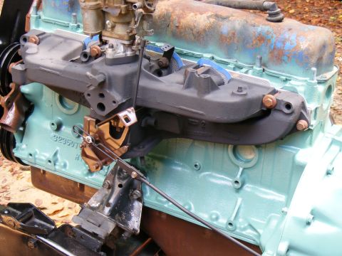 Close-up of an engine block with a carburetor and intake manifold. Some blue paint is visible on the block
