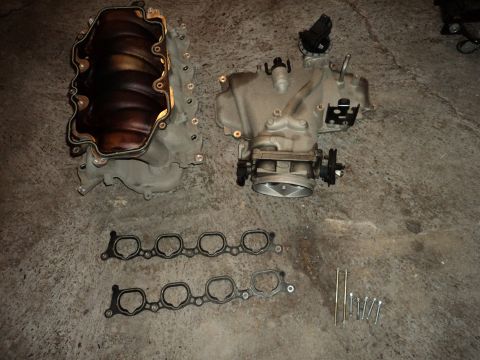 2004 Mercury Grand Marquis - Disassembled engine intake manifold components and gaskets are shown on a concrete surface.