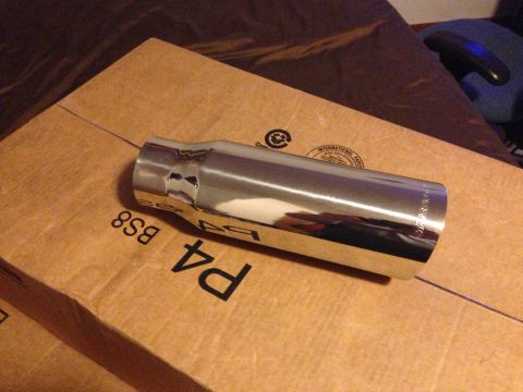 1992 Ford F-150 - A polished chrome exhaust tip with a stepped, rolled-edge outlet rests on a cardboard box stamped "P4 BS8", one side dented near the smalle…