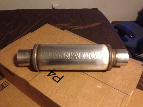 1992 Ford F-150 - Polished stainless Magnaflow performance muffler with dual inlet/outlet pipes sitting on cardboard boxes indoors.