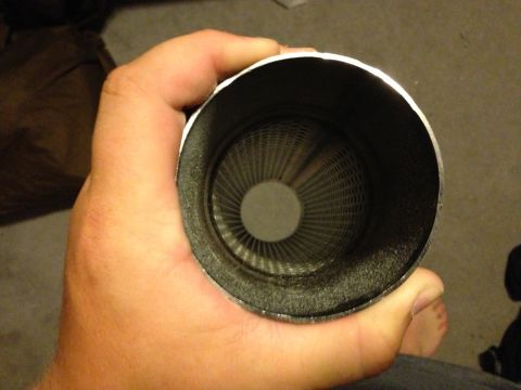 1992 Ford F-150 - A hand holds a cylindrical black exhaust muffler or resonator, viewed straight into the open end to show the perforated inner core and louv…