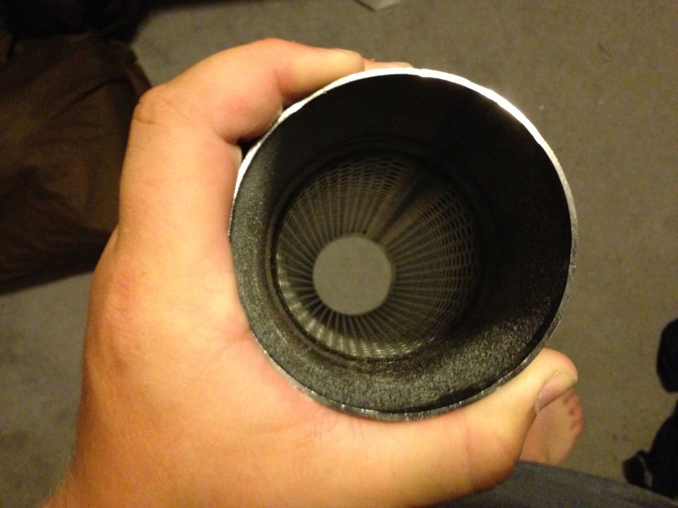 Hand holding a black exhaust muffler, end-on view showing the perforated inner core