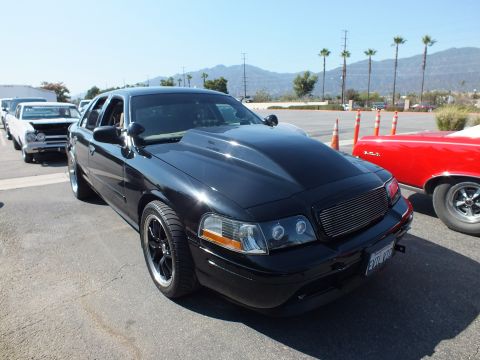 2003 Ford Crown Victoria - blacked-out Ford Crown Victoria sedan with a billet grille and black wheels parked on asphalt, mountains and palms behind.
