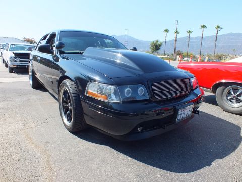 2003 Ford Crown Victoria - Front three-quarter view of a black Ford Crown Victoria sedan with a chrome billet grille, black wheels, and a California license plate.