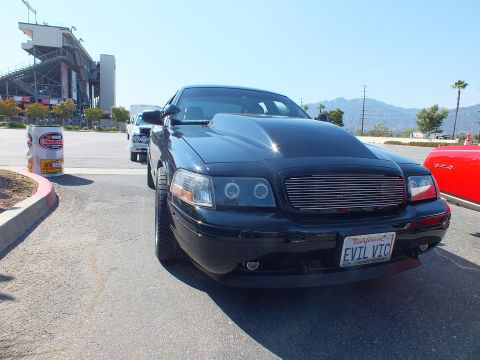 2003 Ford Crown Victoria - black Ford Crown Victoria with halo headlights and billet grille, plate 'EVTL VTC', parked in a lot beside grandstands.