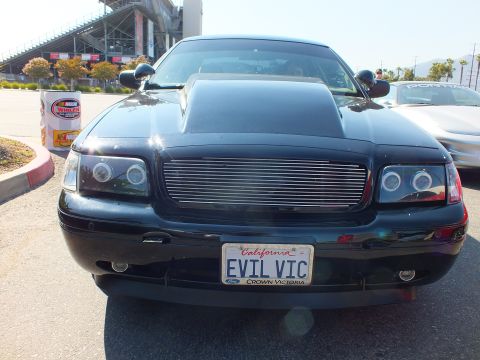 2003 Ford Crown Victoria - Head-on view of a black Ford Crown Victoria with billet grille and halo headlights, wearing a California 'EVIL VIC' plate.