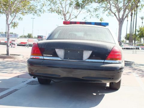 2003 Ford Crown Victoria - Close rear view of a black Ford Crown Victoria police interceptor with a red-and-blue roof light bar and chrome bumper.