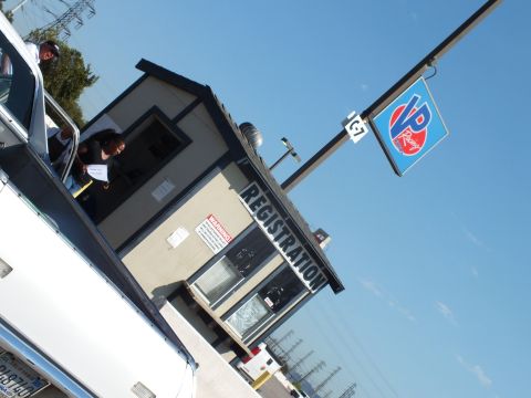 2003 Ford Crown Victoria - tilted view of a building with a 'REGISTRATION' banner and a VP Racing Fuels flag, people standing at the entry near a vehicle.