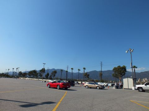 2003 Ford Crown Victoria - wide nearly empty parking lot holds a red convertible and a few tan sedans, with palms and a mountain range in the distance.