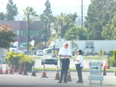 2003 Ford Crown Victoria - Two people stand talking among orange traffic cones beside a 'KEEP RIGHT' arrow sign, cars and palms in the hazy background.