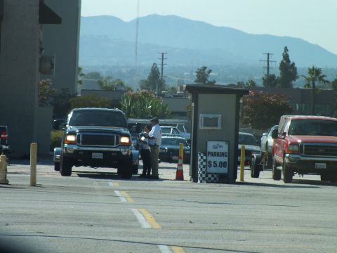 2003 Ford Crown Victoria - black Ford Super Duty pickup pauses at a checkered '$5.00 parking' booth attendant, with a red truck and mountains beyond.