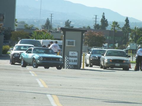 2003 Ford Crown Victoria - teal vintage Mustang and other cars line up at a checkered '$5.00 parking' booth while attendants in white shirts direct them.