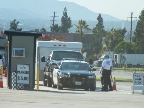 2003 Ford Crown Victoria - black sedan and dark pickup pass a $5.00 parking booth and a KEEP RIGHT sign as staff direct traffic.