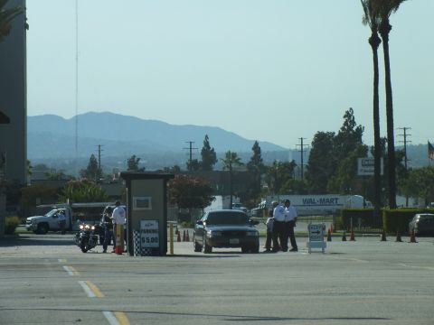 2003 Ford Crown Victoria - motorcycle and sedan enter past a $5.00 parking booth near a Wal-Mart sign with mountains in the background.