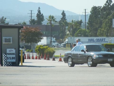 2003 Ford Crown Victoria - dark gray Ford sedan rolls past a $5.00 parking booth lined with orange cones, Wal-Mart semi trailers behind.