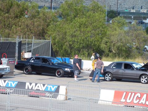 2003 Ford Crown Victoria - black Ford Crown Victoria marked with numbers sits behind MAVTV banners as spectators gather at a drag event.