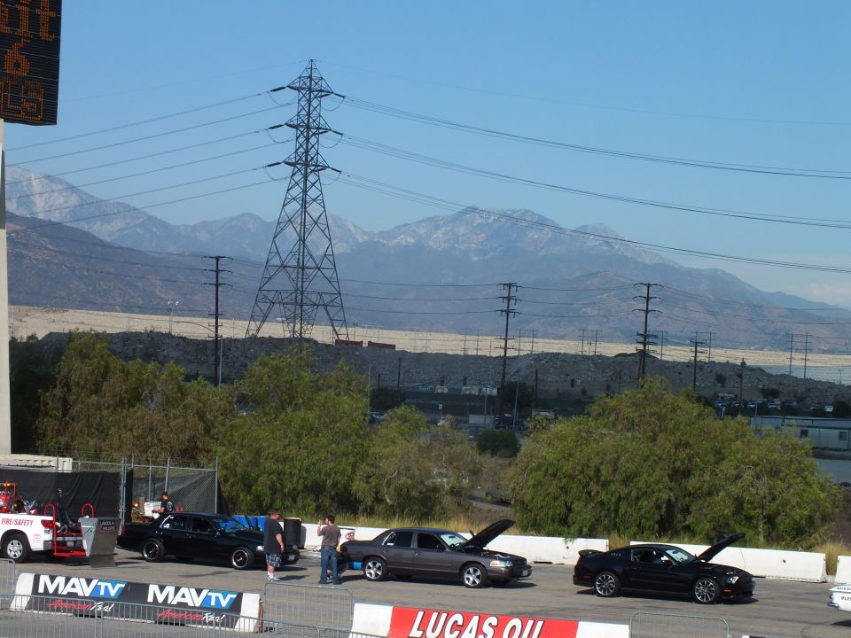 Distant staged cars below a transmission tower and snowy mountains behind MAVTV banners