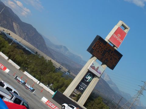 2003 Ford Crown Victoria - angled shot of a Toyota and Irwindale pylon flashing STREET LEGAL DRAG RACING above an event lot and mountains.
